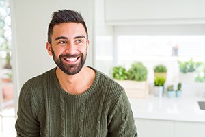 Man in green sweater sitting in kitchen and smiling