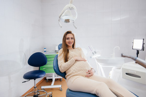 Pregnant woman sitting in a dental chair and smiling