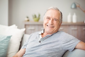 Senior man in collared shirt sitting on couch and smiling